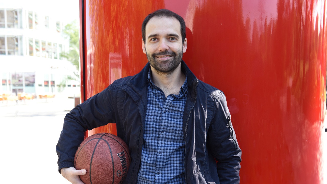 Man in leather jacket and basketball standing in front of red background.