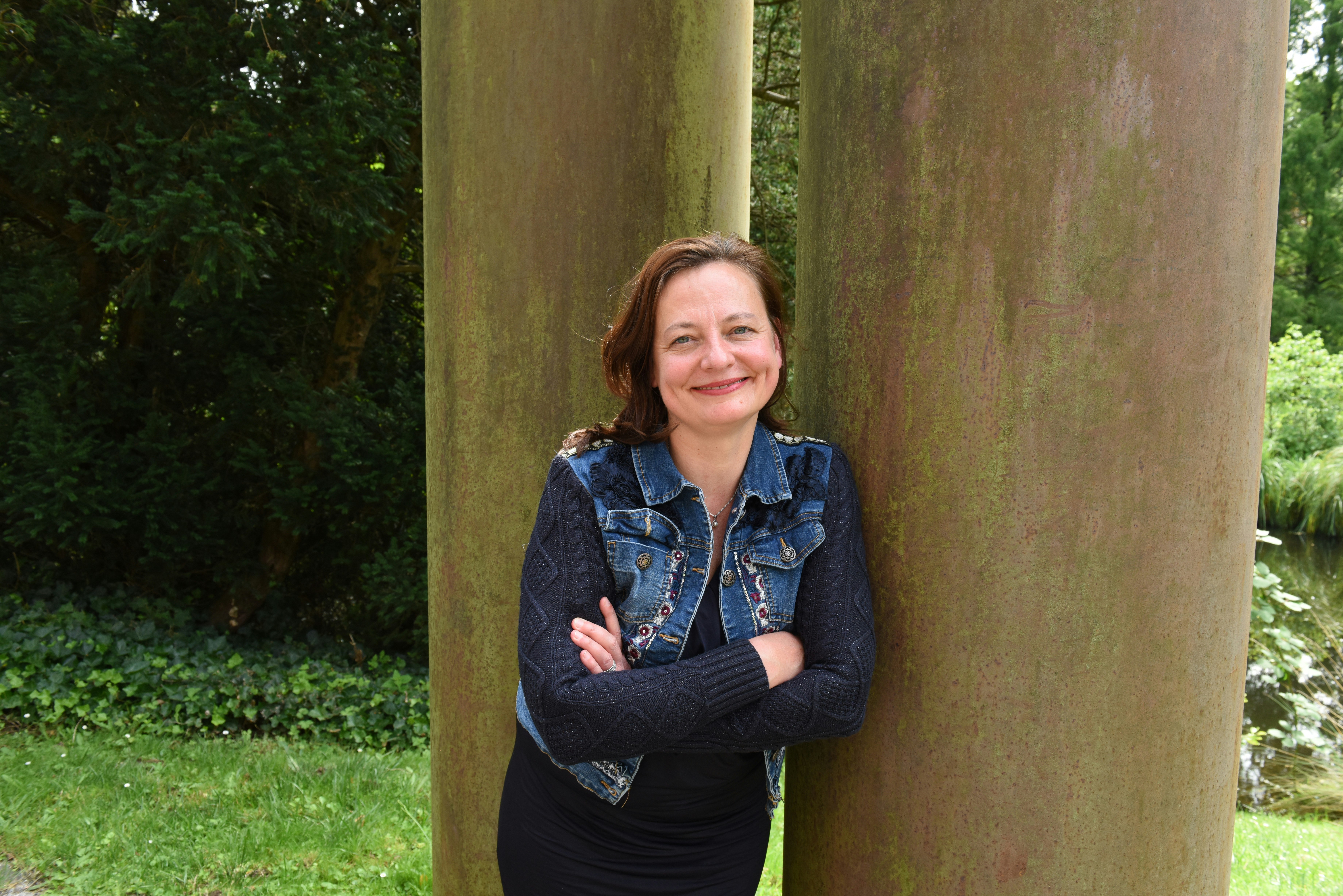 Susanne smiles and leans against a tree.