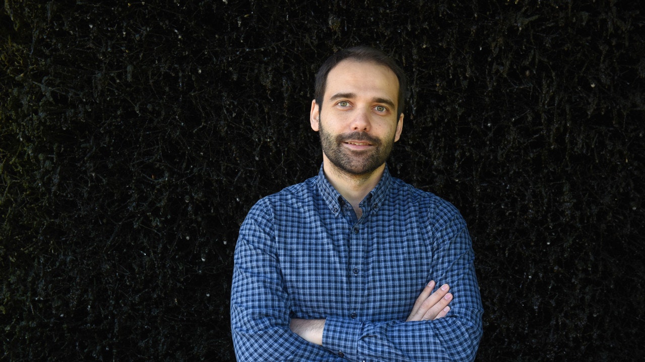 A man in a checked shirt holds his arms crossed.