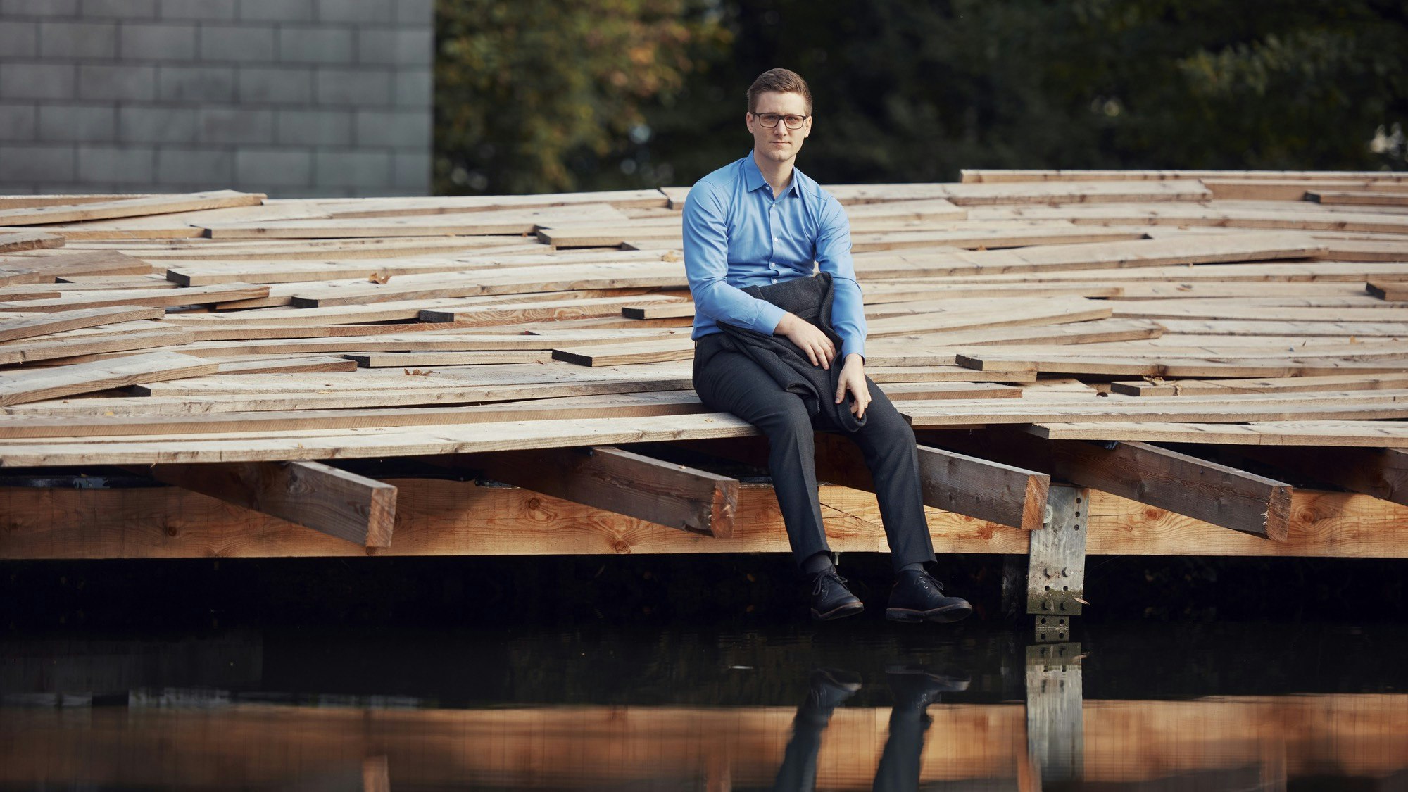 Man in suit sitting on a wooden dock.