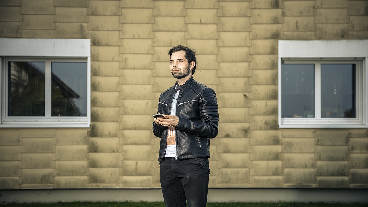 Mann in Lederjacke steht draussen mit seinem Mobile in der Hand.