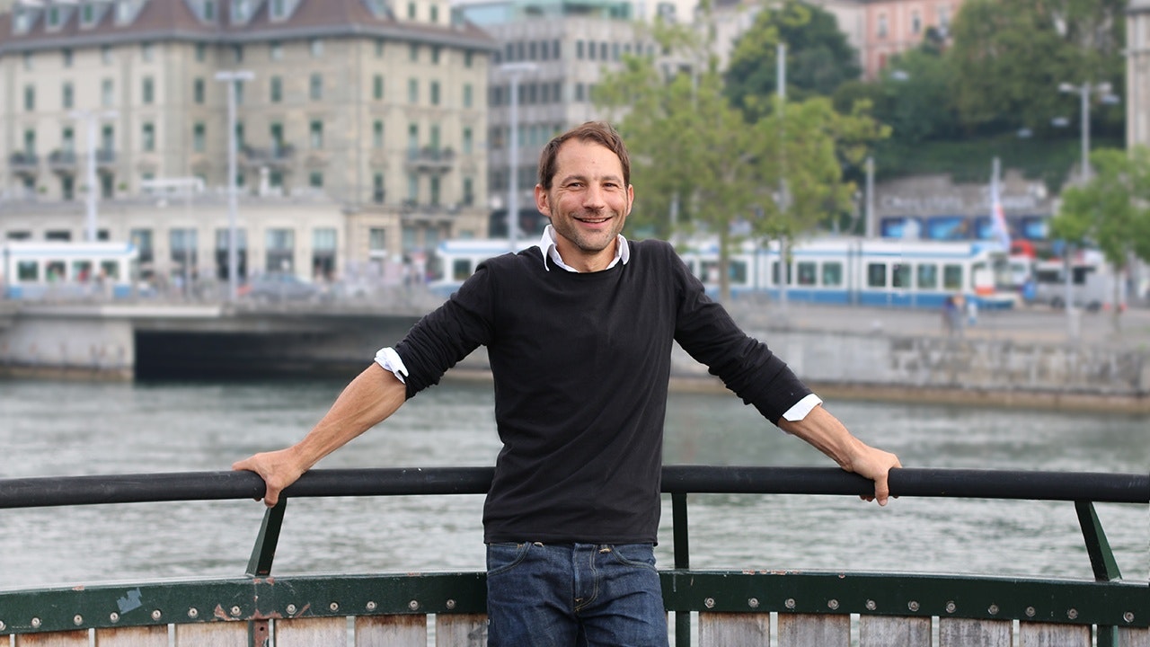 A man stands by the river in front of a city backdrop.