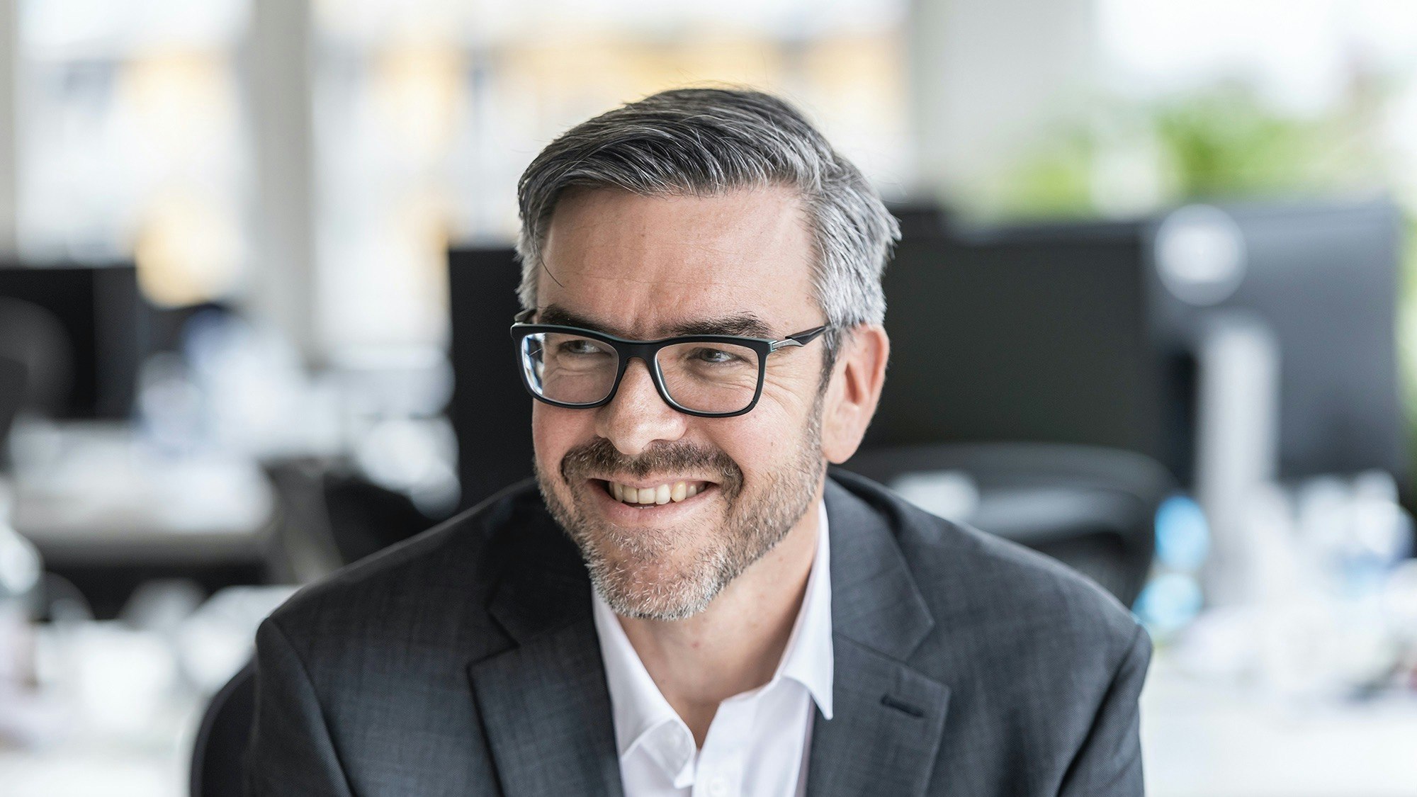 Man with glasses laughing and looking sideways.