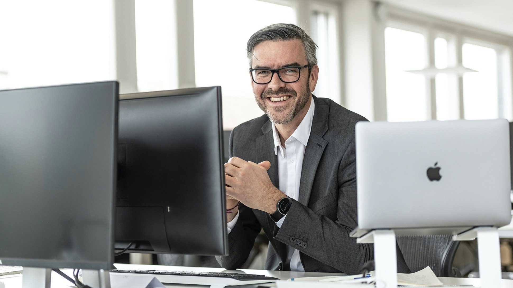 Daniel Darioli sitzt an einem Schreibtisch in einem Büro, zwischen seinem Laptop und einem Bildschirm.