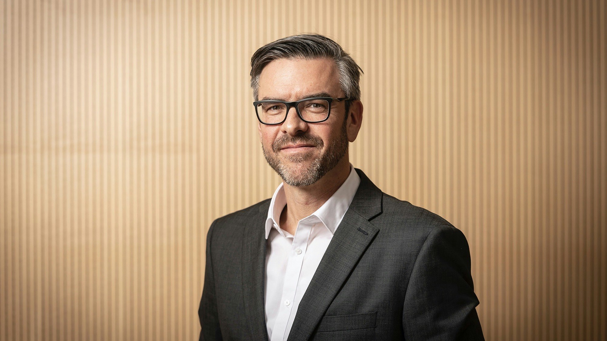 Man in suit in front of wooden wall.