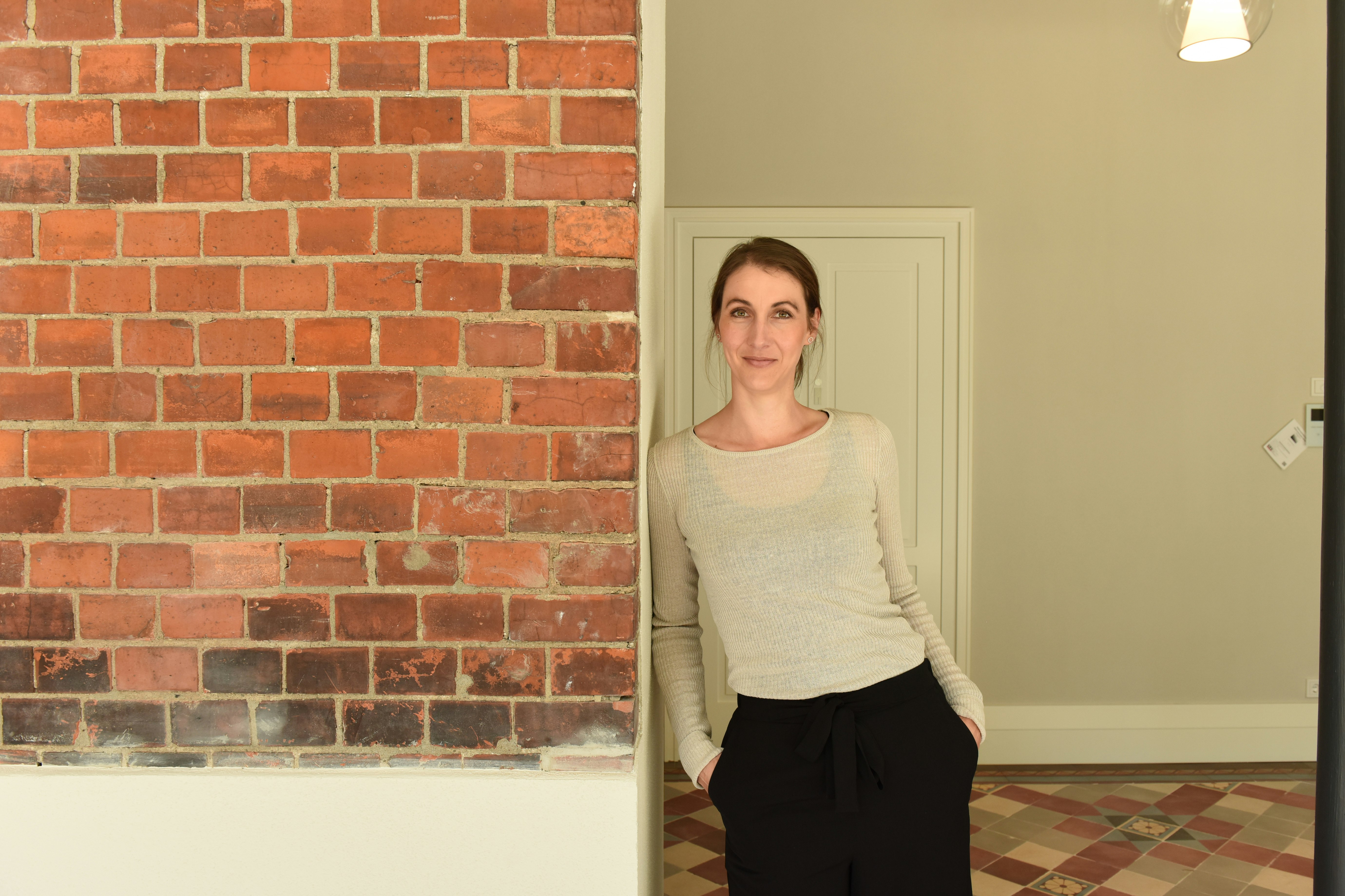Katrin leans against a brick wall.
