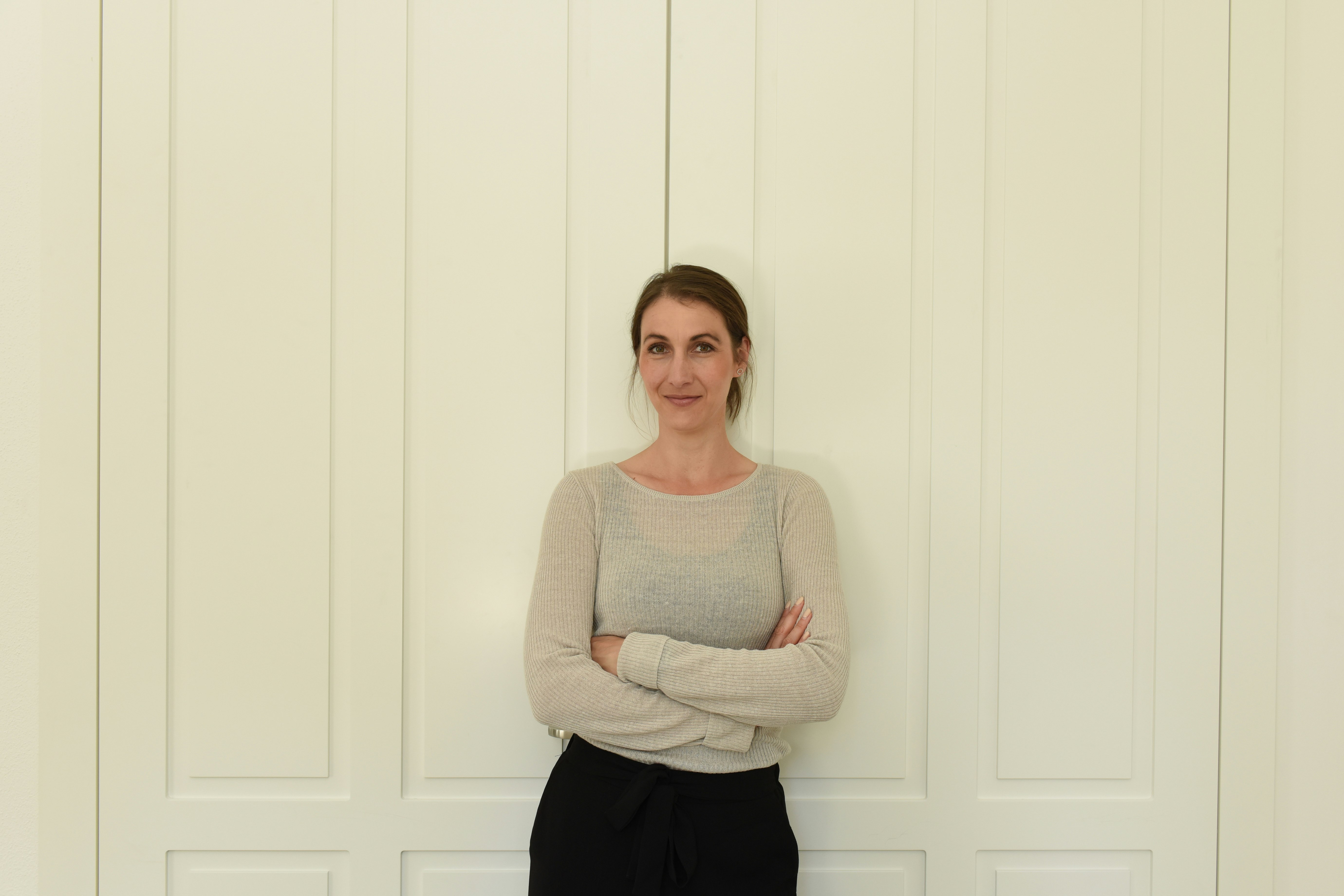 Katrin stands in front of a door with her arms crossed.