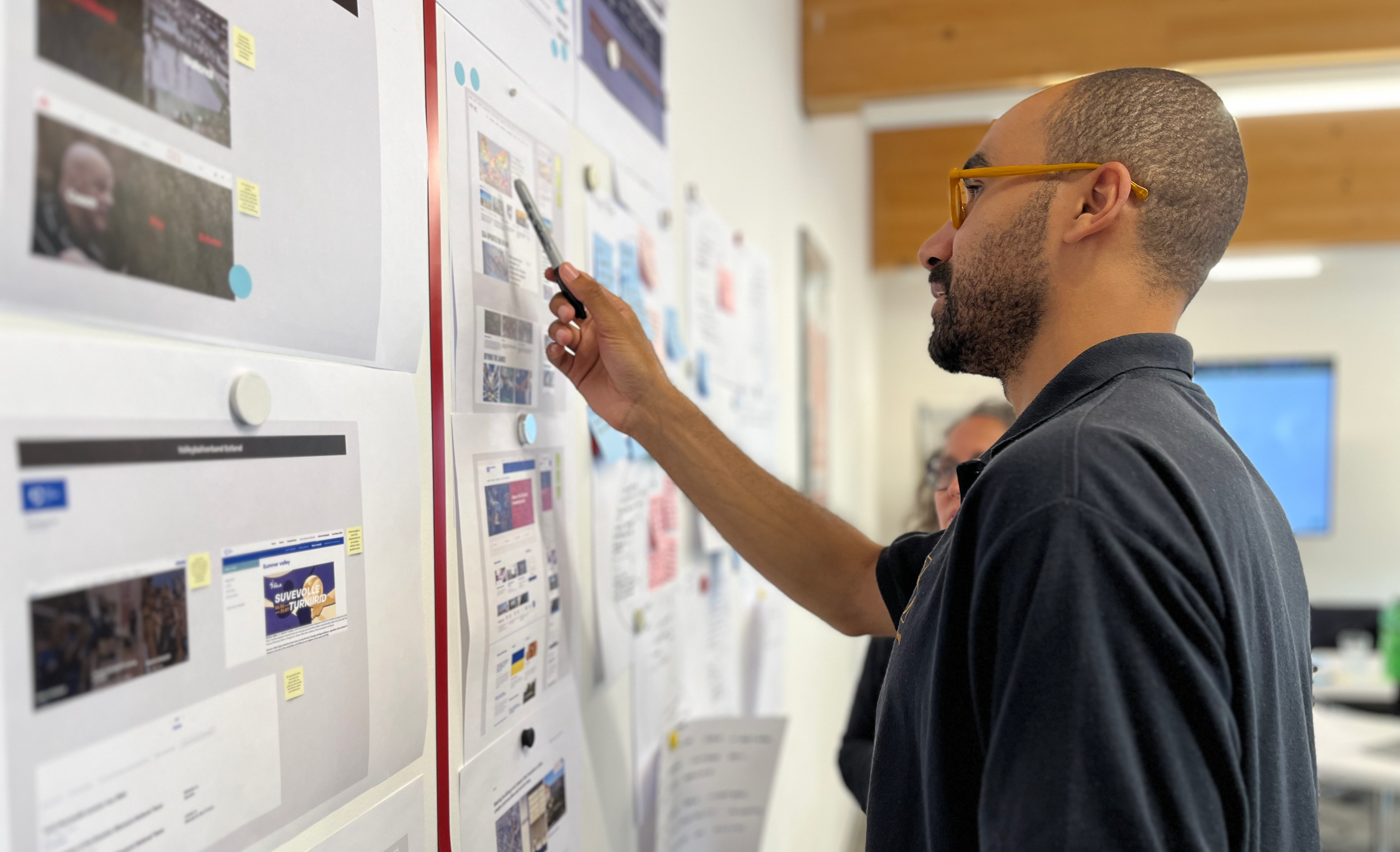 Der Designer David zeigt auf Bildschirmentwürfe auf einem Whiteboard, die Ideen und Konzepte illustrieren.