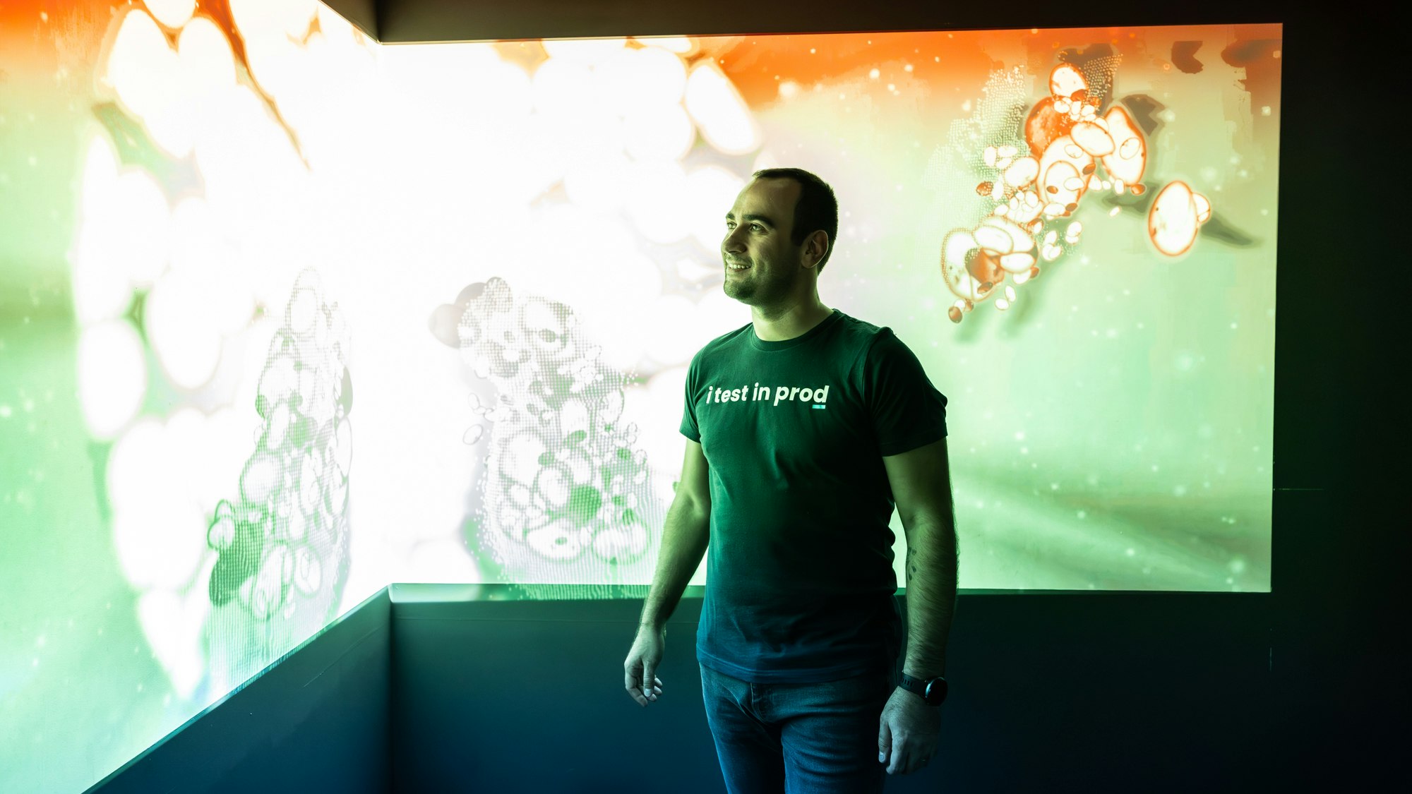 A man in a shirt saying "I test in prod", standing in front of a screen projection