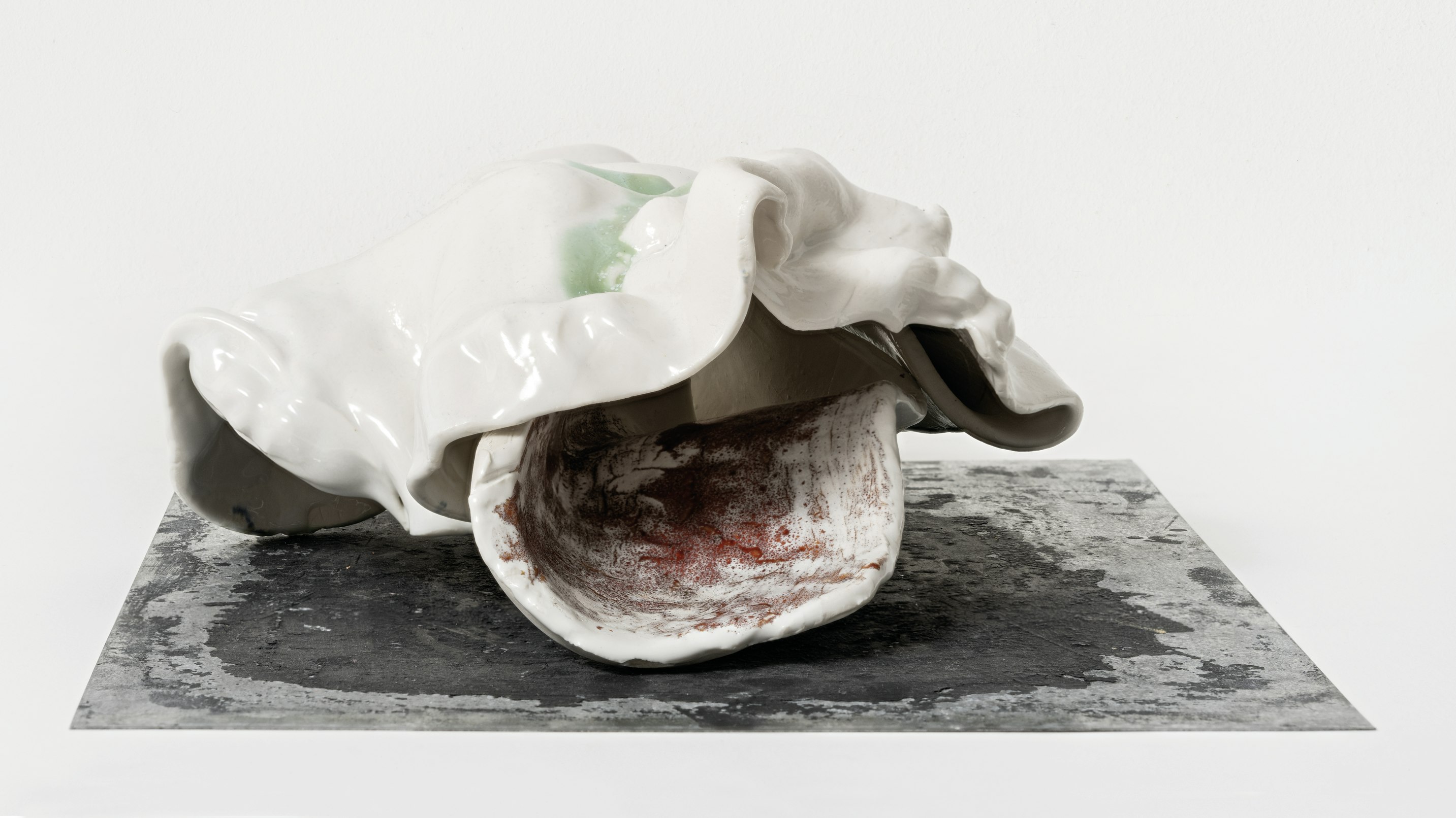 a mostly white ceramic sculpture in the shape of a seashell with glazed surface
