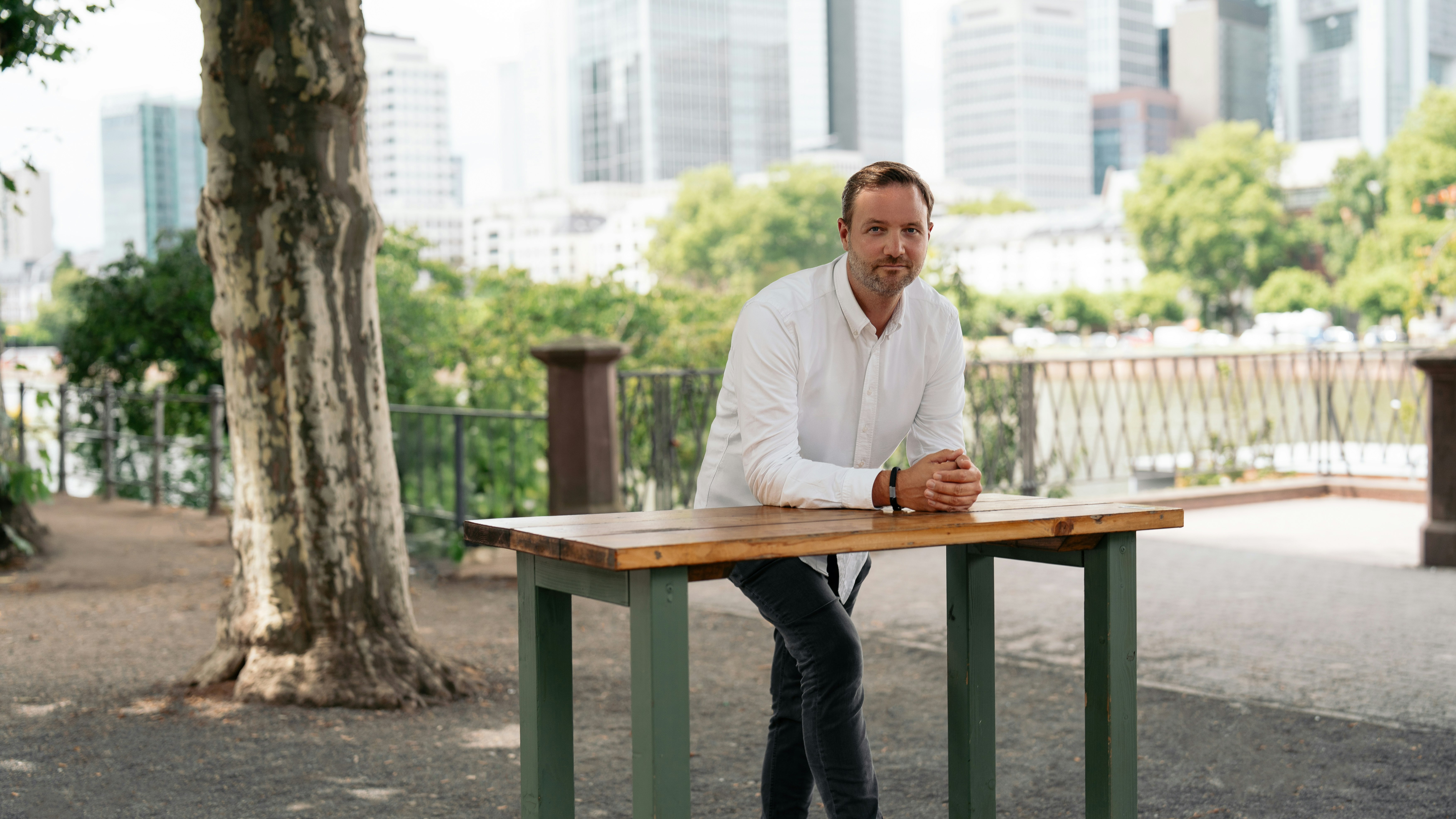Sebastian Immer sitzt an einem Tisch im Freien und lehnt sich mit verschränkten Händen nach vorne.
