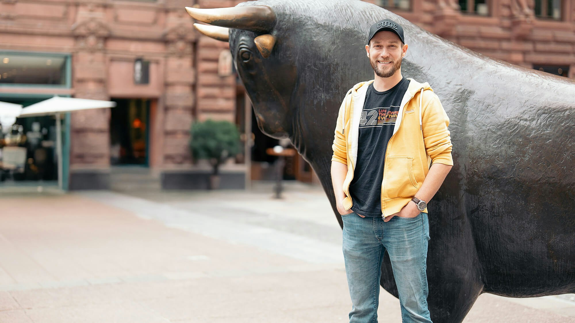 Michael Lemler steht vor einer großen Bullenskulptur in einer Stadt