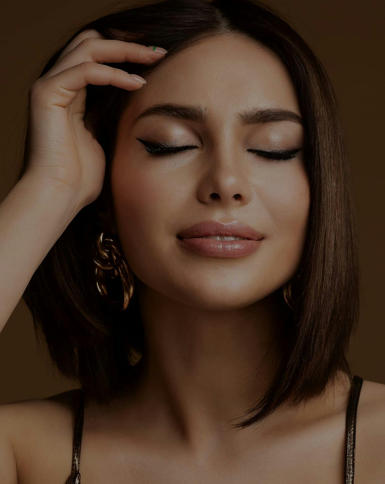 Smiling woman with her eyes closed brushing hair out of her face.