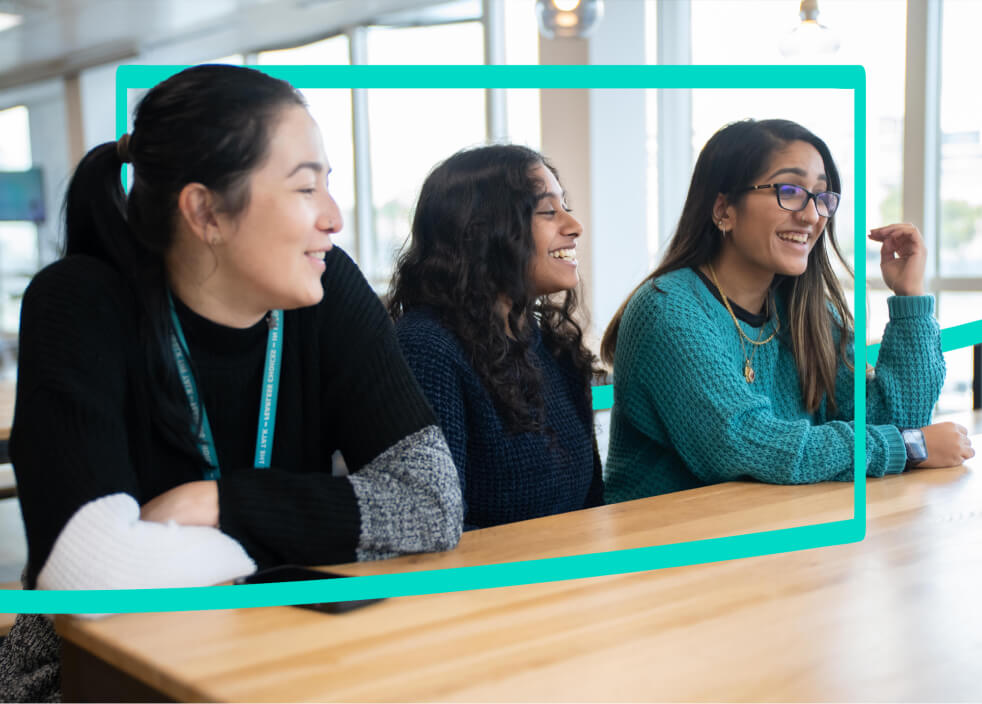 3 women sat a desk laughing looking away from the camera