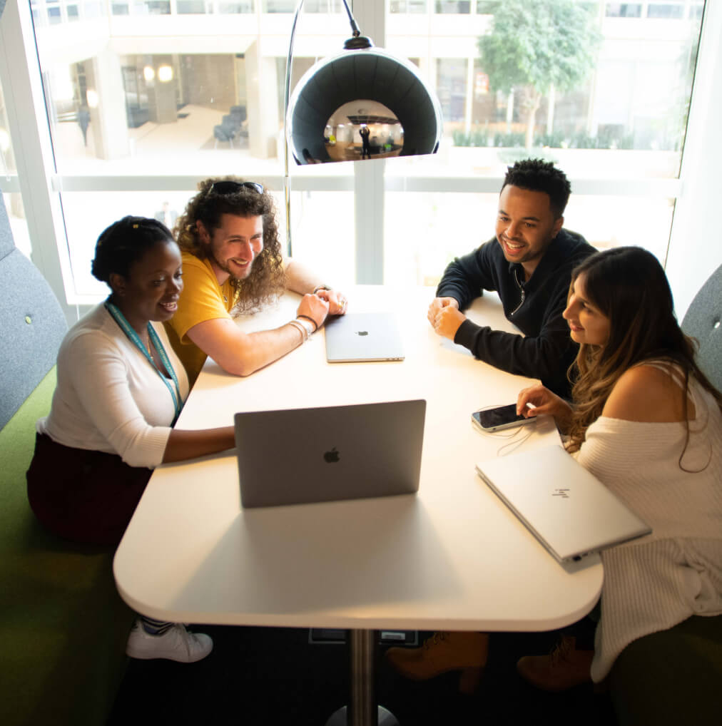 A group of 3 women and a man sat looking at 1 laptop