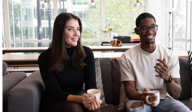 A man and woman sat drinking from mugs on a sofa