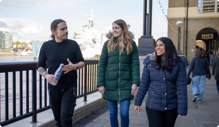 A man and two woman walking along the Thames.