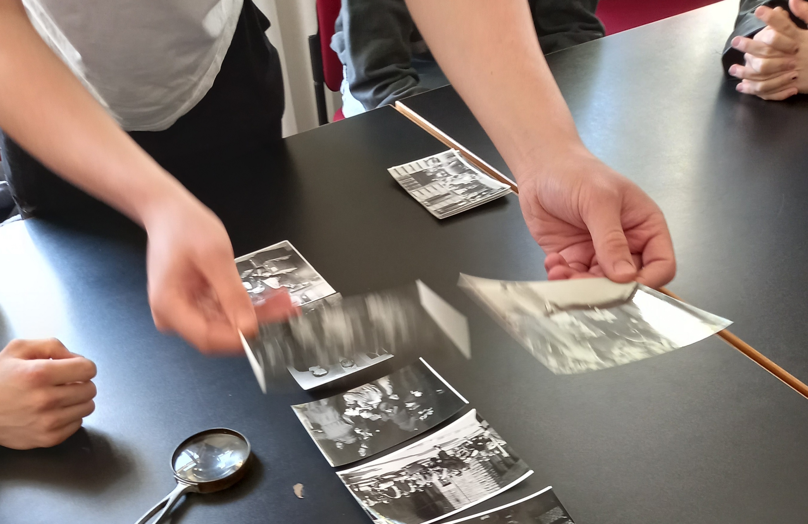 Das Foto zeigt Fotos auf einem Tisch, und Hände, die die Fotos sortieren.