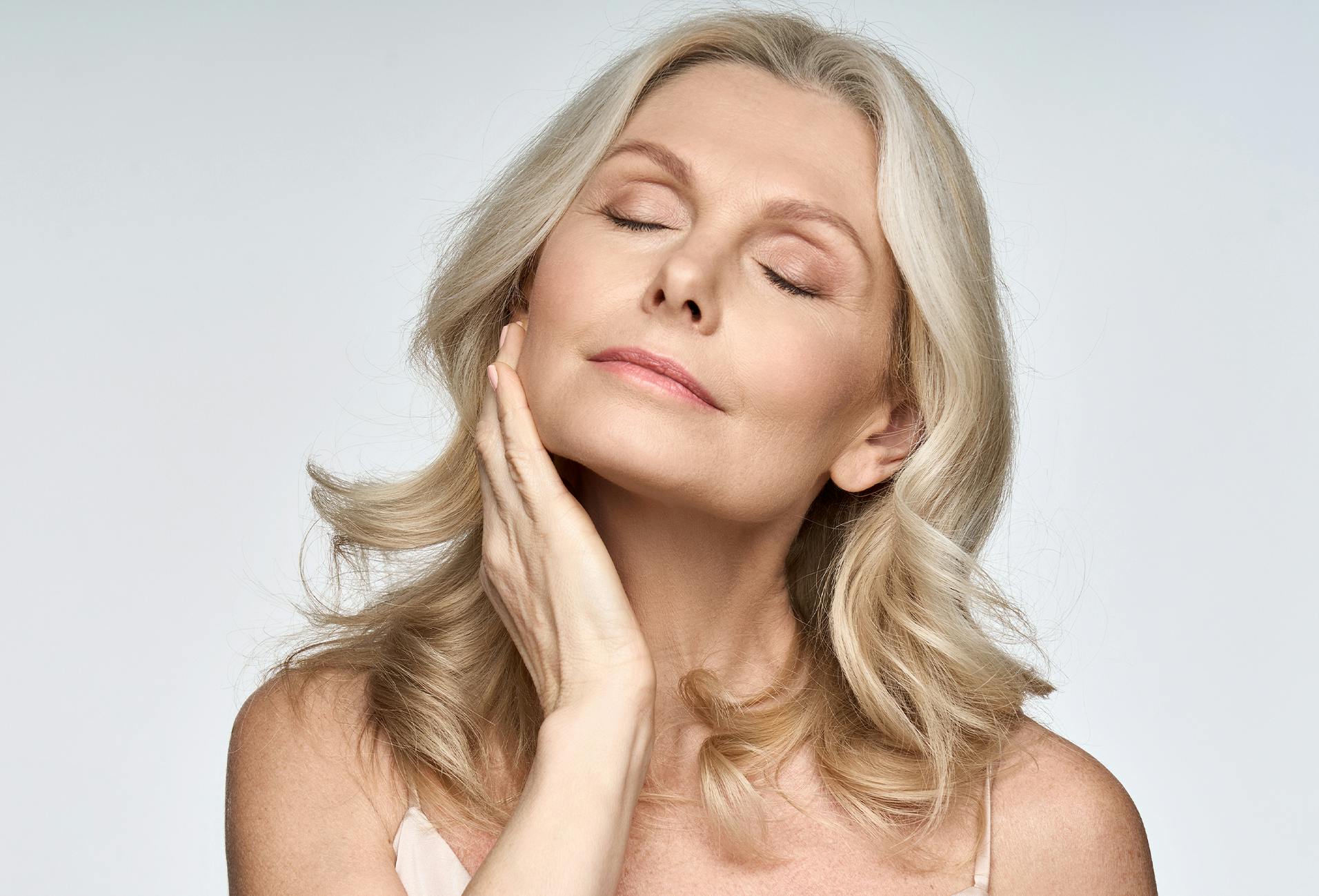 Beautiful middle aged woman with curly blonde hair touching her face with her eyes closed