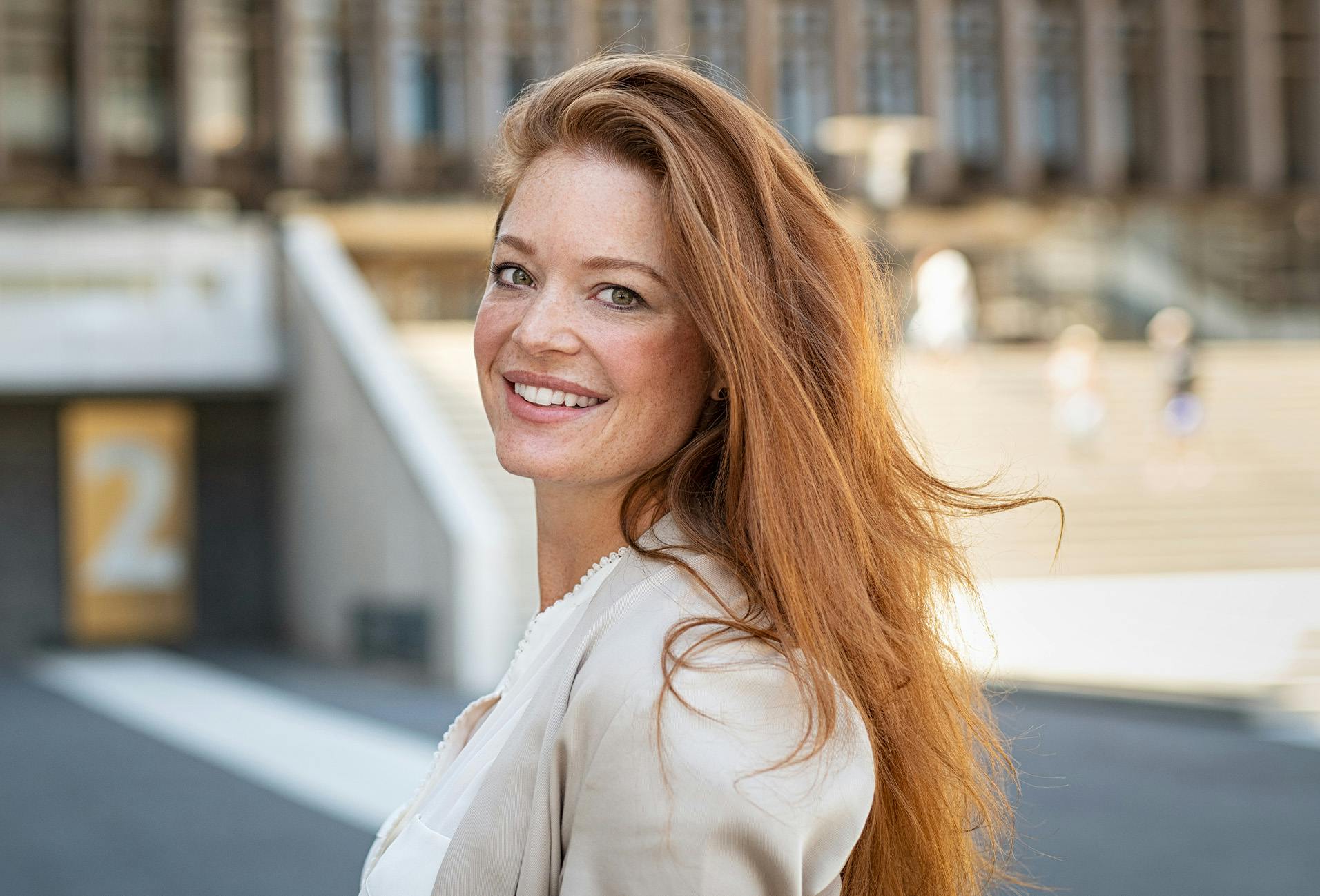 smiling woman with long red hair in a city setting