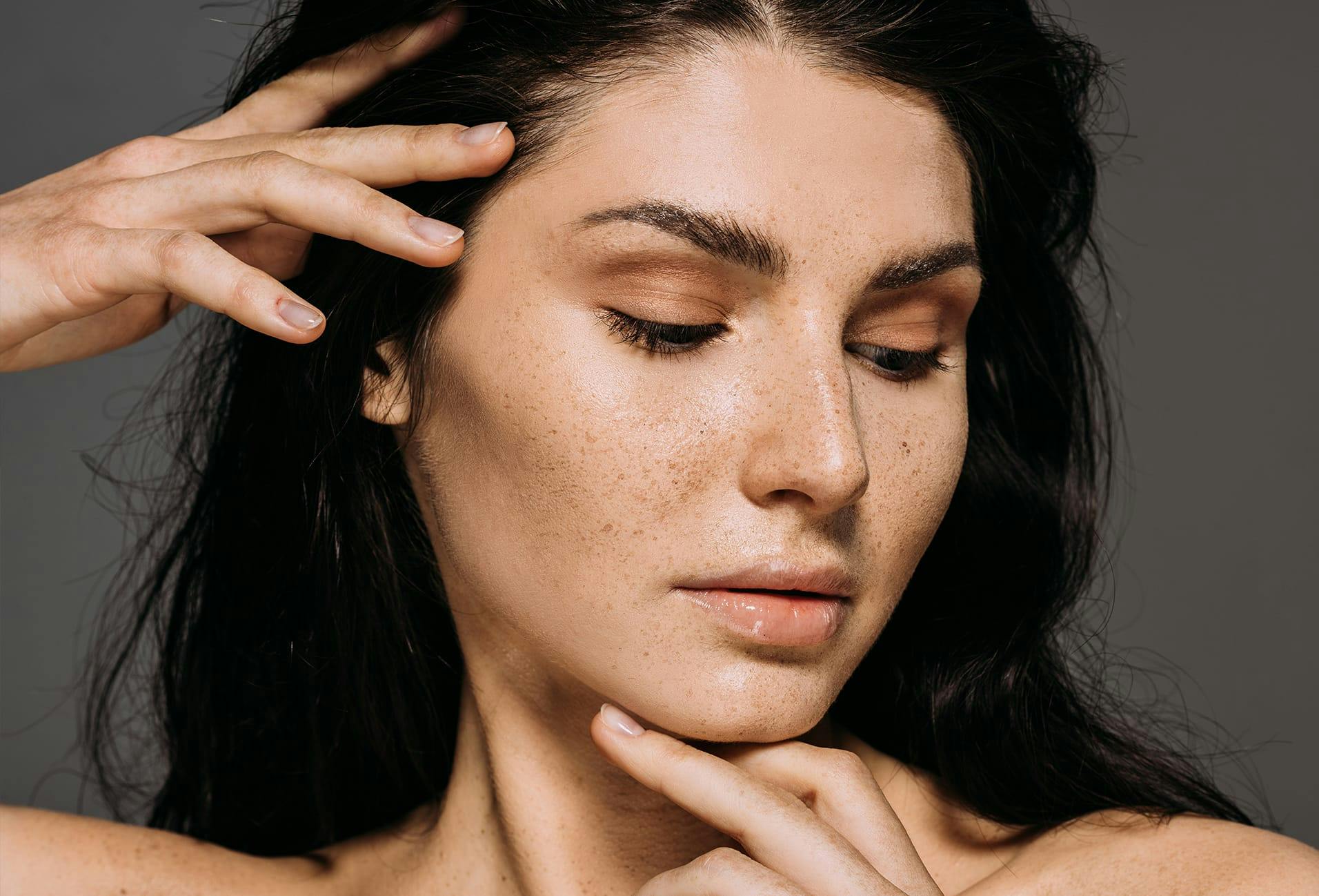 Woman with freckles looking to the side while touching her face