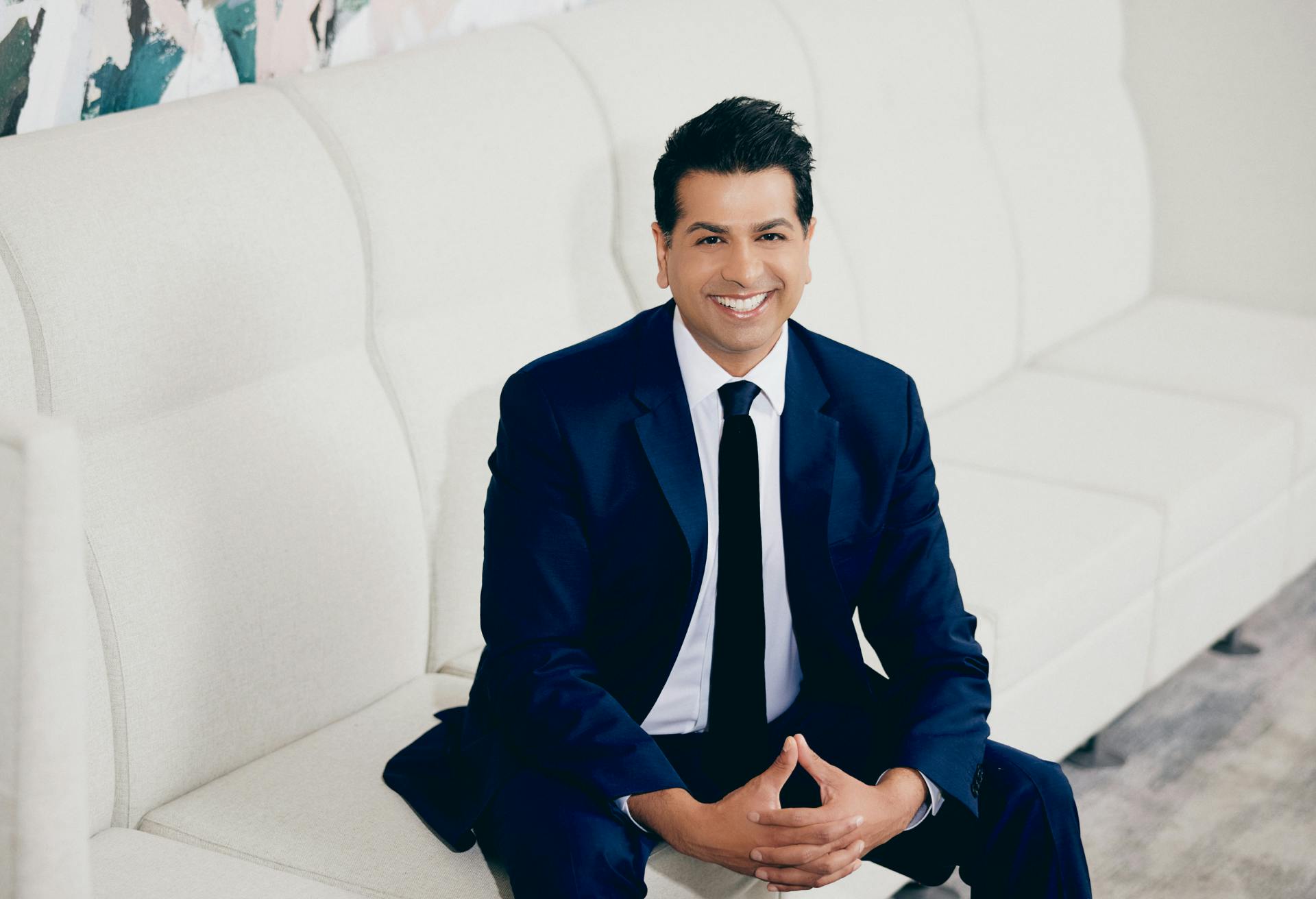 Dr. Neil Tanna in a suit sitting on a white couch