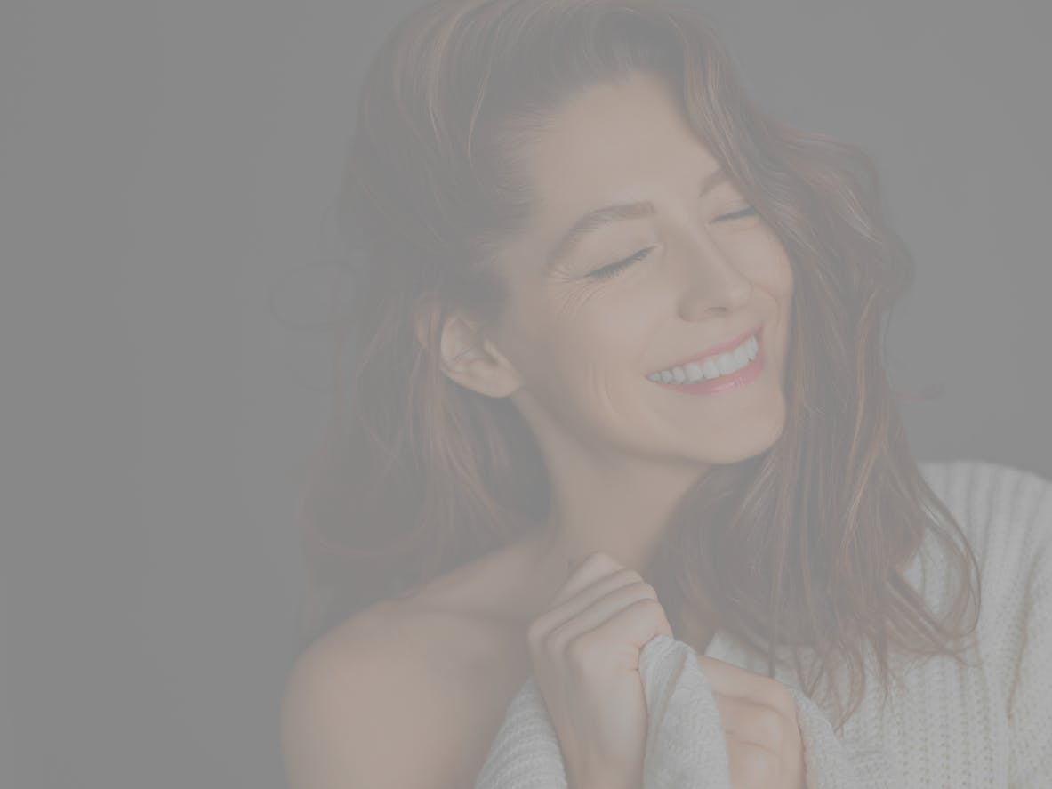 Older woman with brown hair smiles with eyes closed in studio shoot to show potential results of a facelift in Long Island with Dr. Tanna