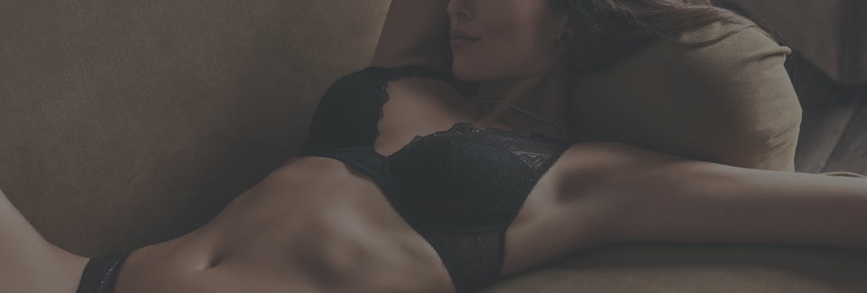 woman laying on couch in lingerie. Arms above head showing off what could emulate the results of a breast reduction in Long Island