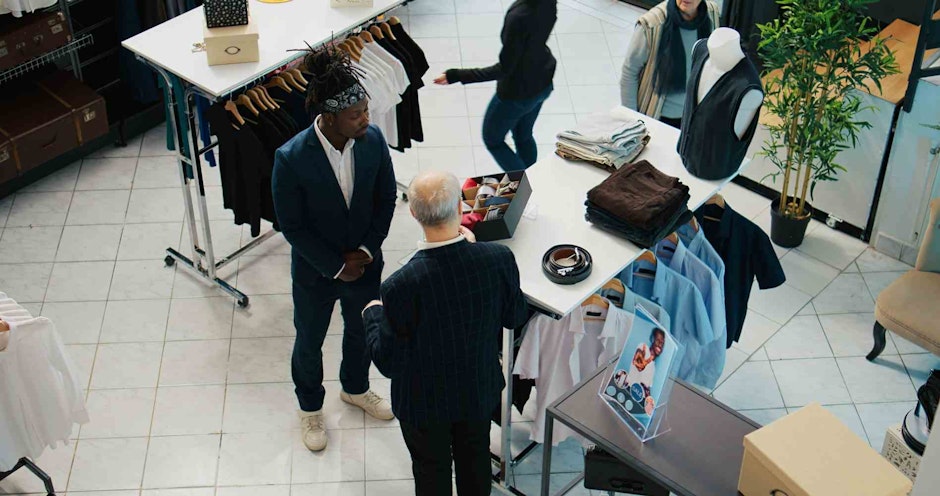 Senior designer teaching his apprentice to match ties on elegant suits, presenting the color mixing theory to his pupil