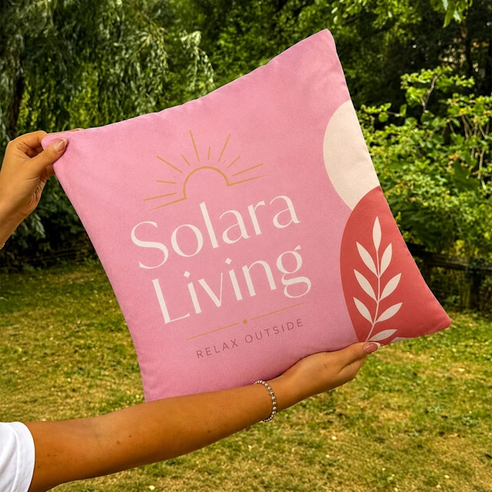 Pink custom printed branded cushion with full colour Solara Living design displayed outdoors