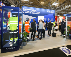 An Exhibition stand for Alsico, uniforms displayed in cases at the front while people talk in a group behind.