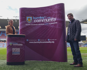 Two people standing, at Turf Moor Stadium, next to a magnetic pop up display which includes Burnley FC branding.