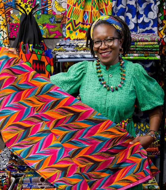 A Lady, in a green dress, proudly showing her colourful Quilt.