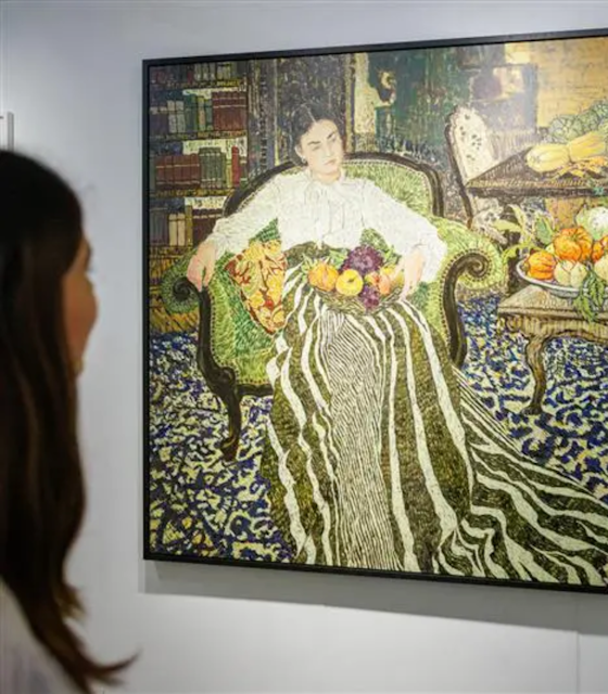 A lady onlooking an art piece of a woman sat on a chair with fruit in her lap.