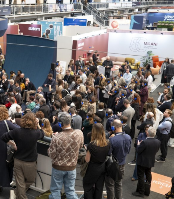Image of a large group of people, all with headphones on, listening to a talk in a large exhibition hall.