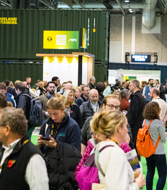 A green exhibition hall with a lot of people stood and chatting.