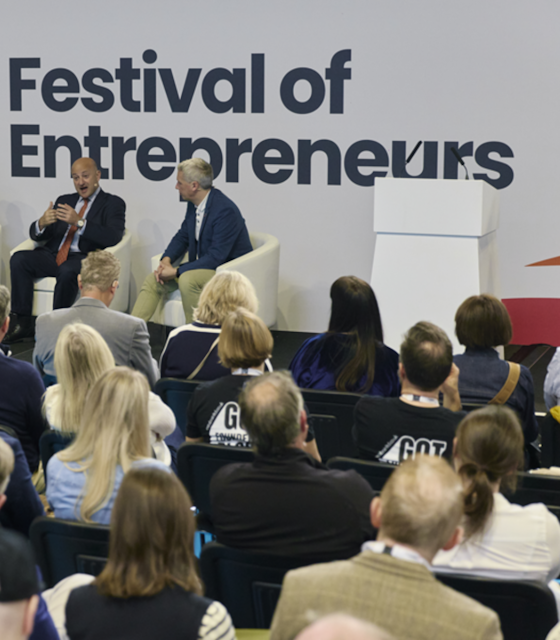 Two men sat giving a talk on a stage with the Phrase Festival of Entrepreneurs in the backdrop.