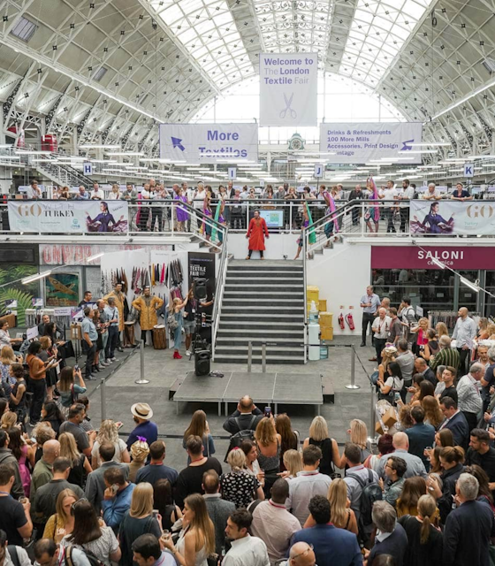 A Large exhibition area with a set of stairs at the centre piece. Large groups of people surround the base of the stairs.