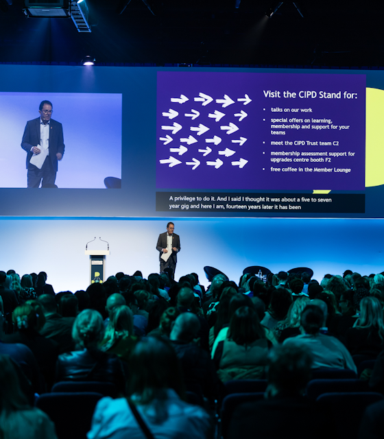 A Speaker at the CIPD giving a talk on stage to a large hall of people.