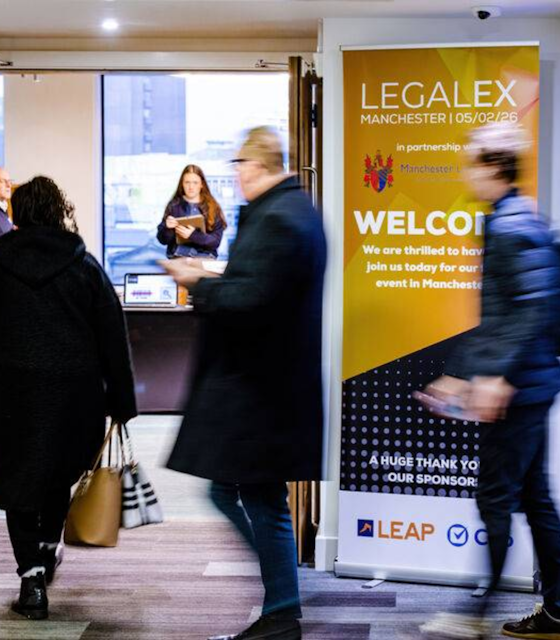 Two blurred people walking infront of a LegalEx Roller Banner.