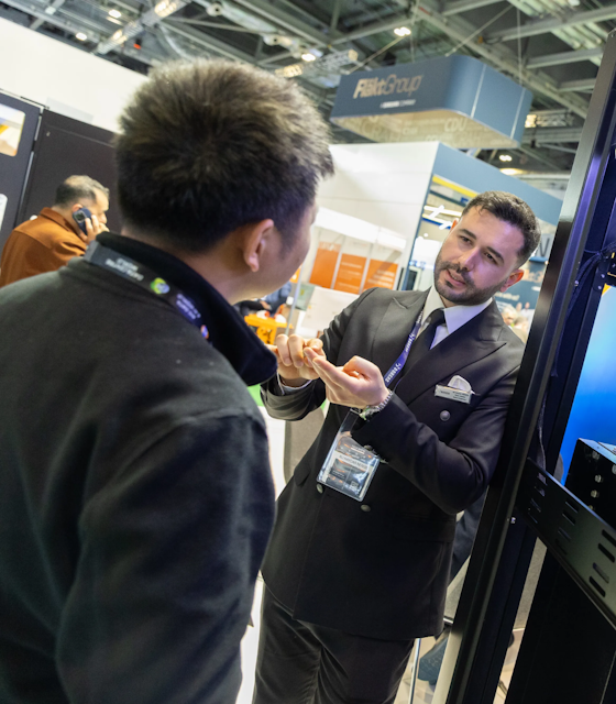 Two business men conversing next to a heavy machine at an exhibition.