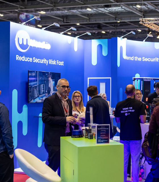 Man stood exhibiting his brand with a blue stand at the DevOps Live exhibition.