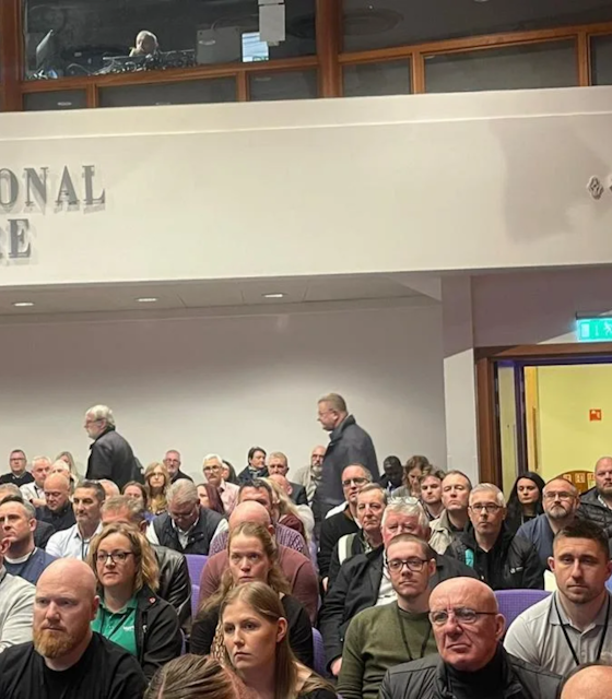 People sat down in a theatre hall intensely listening to a speaker offscreen.