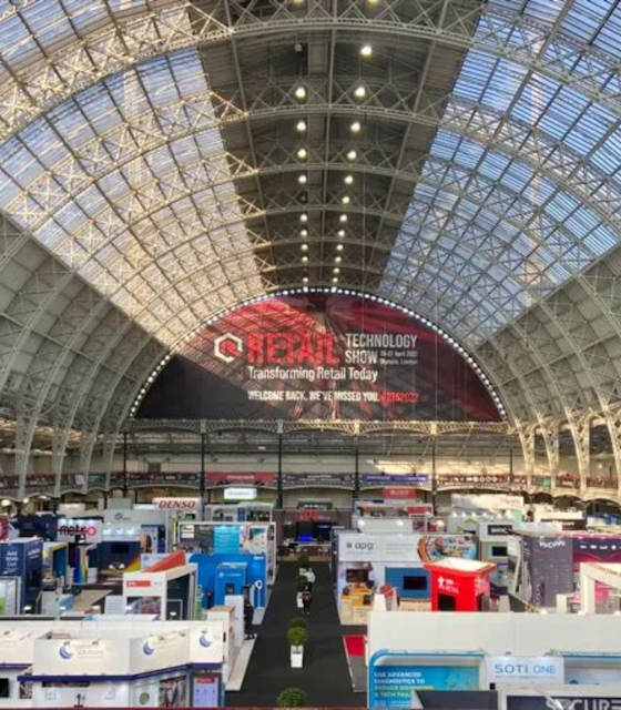 A Large exhibition hall view with a semicircle banner with Retail Technology written.