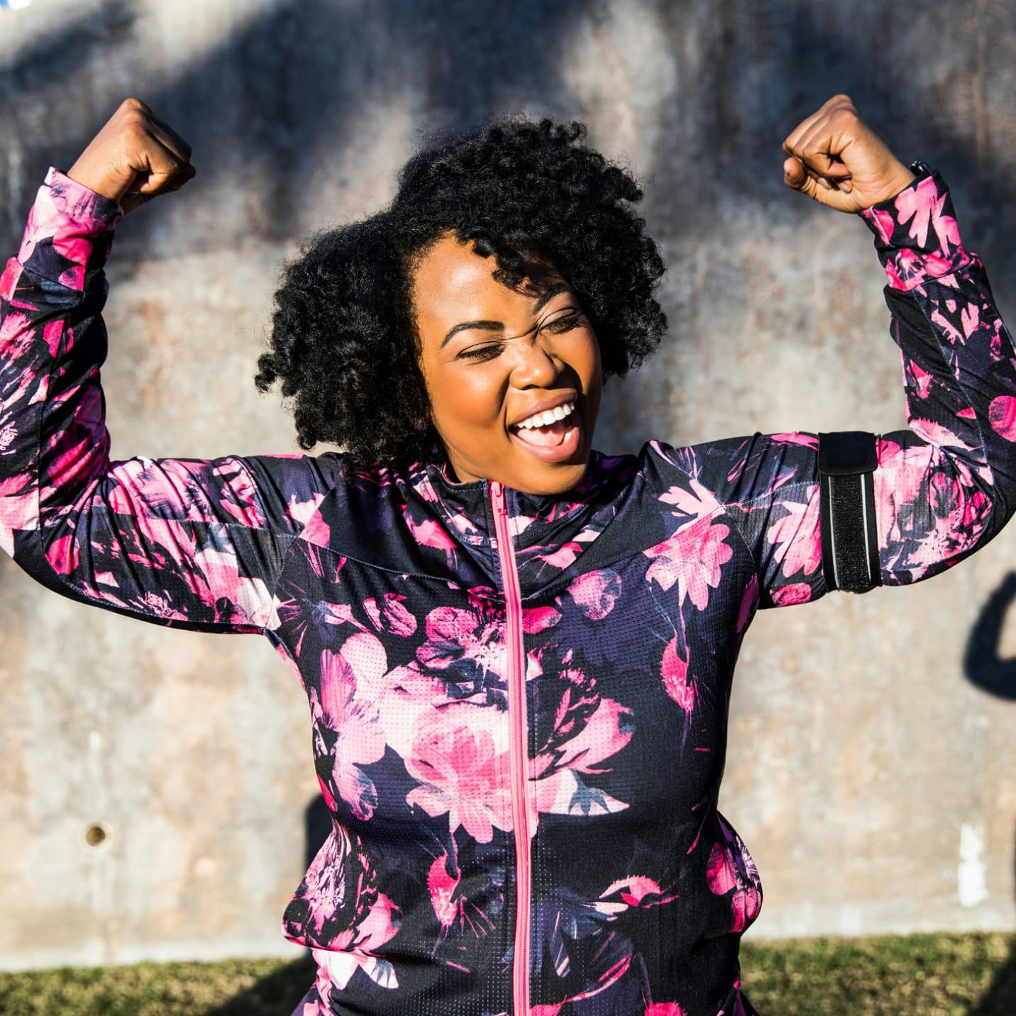 Woman holding her arms up flexing while smiling.
