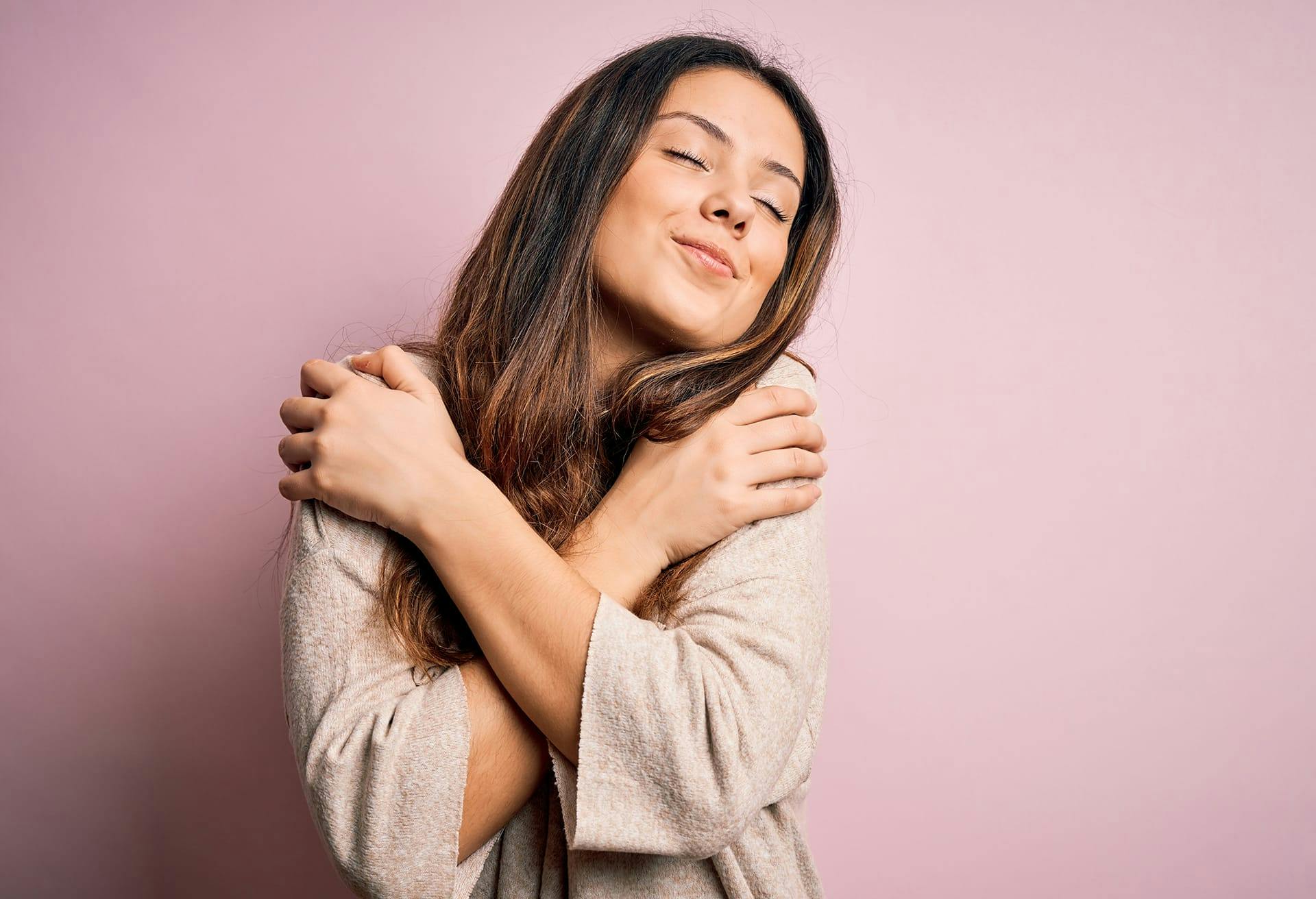 Woman crossing her arms in front of her chest in front of a lavender wall