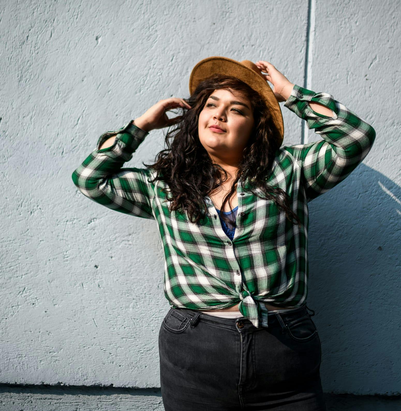Woman wearing a hat resting against a concrete wall
