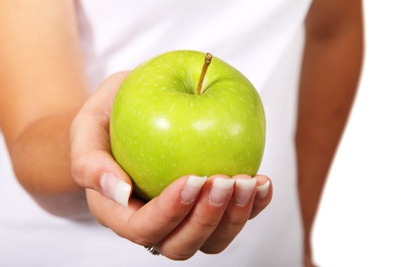 someone holding a green apple in their hands on a white background