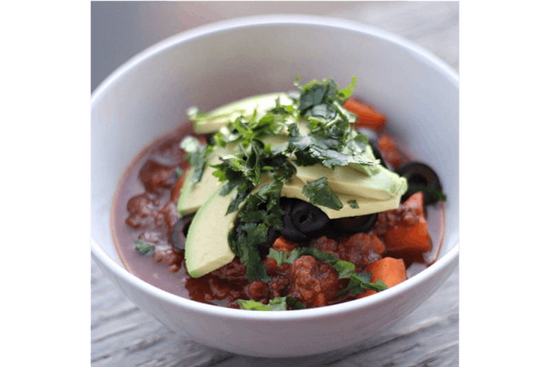 there is a bowl of chili and avocado with a spoon