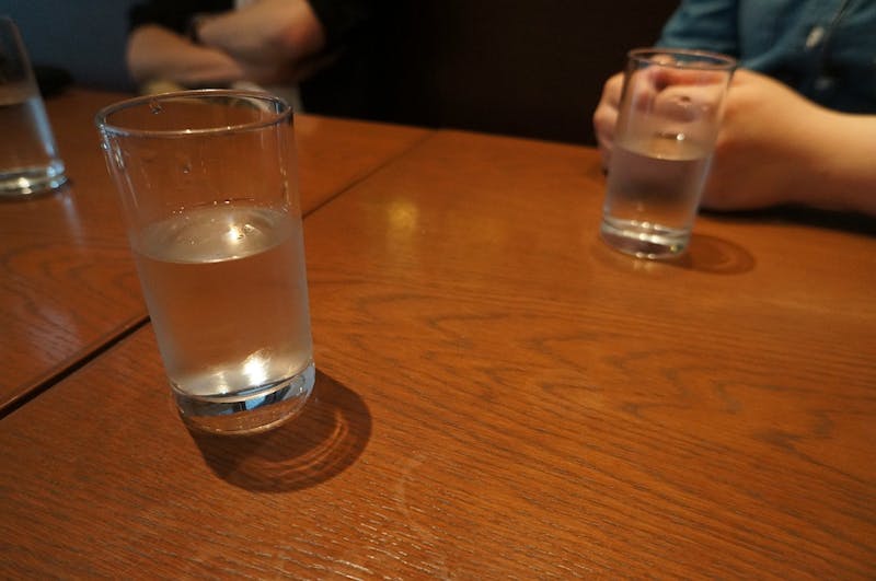 there is a glass of water sitting on a table with a person sitting in the background